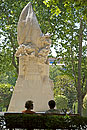 2 women sitting on bench by Statue